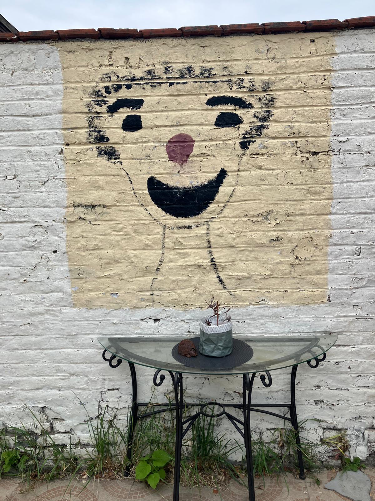 Visage de clown peint sur un mur en briques blanchies, au-dessus d'une table de jardin