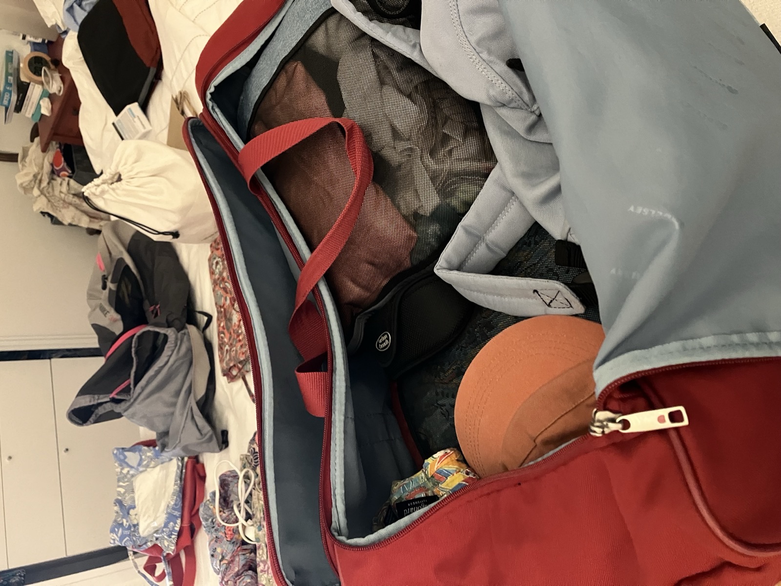 Valise rouge ouverte et remplie sur un lit, entourée d'autres bagages en cours de préparation